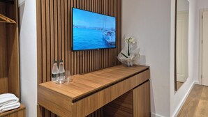 Une salle de bain moderne avec un meuble-lavabo en bois, un téléviseur à écran plat fixé sur un mur recouvert de panneaux en bois, un vase avec des fleurs blanches et un miroir.