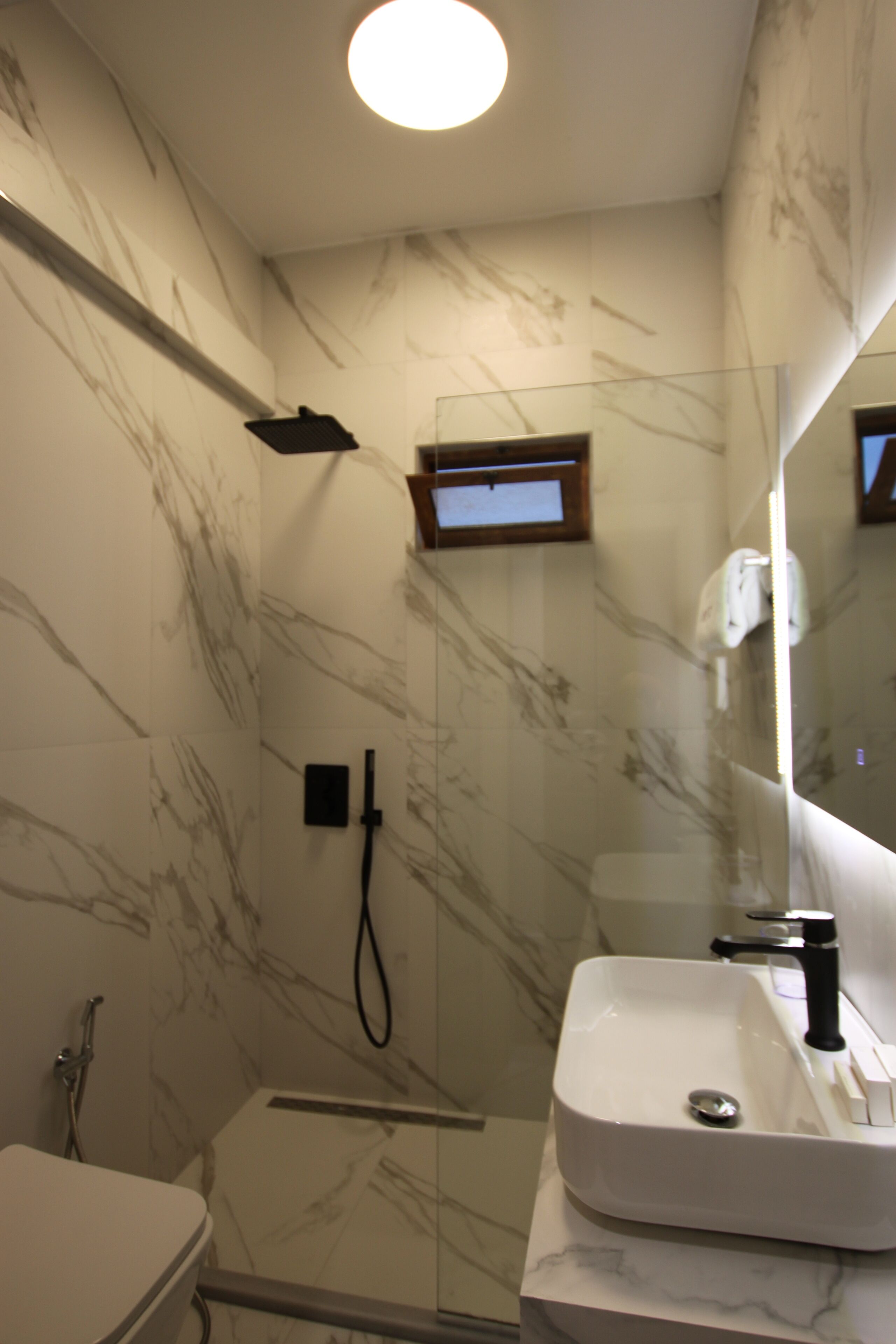 A bathroom with a glass shower enclosure, a white sink, and a marble-patterned wall.