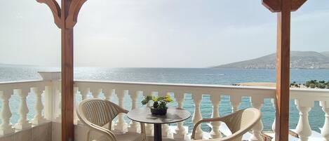A covered outdoor seating area with a table and two wicker chairs, overlooking a coastal view.