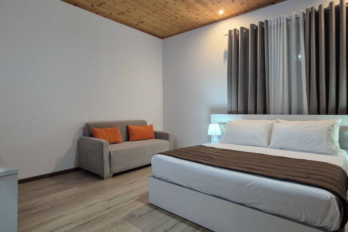 Un dormitorio con cama, sofá, suelo de madera y techo de madera.