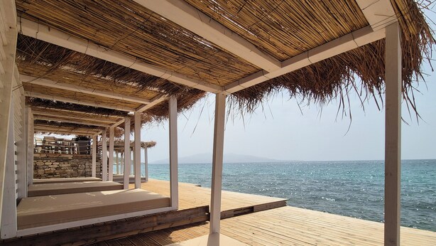 Une terrasse en bois surmontée d’un toit de chaume, avec vue sur la mer.