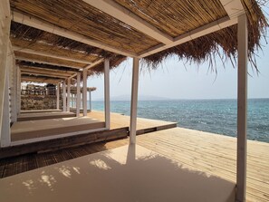 Una terraza de madera con techo de paja, con vistas al mar.