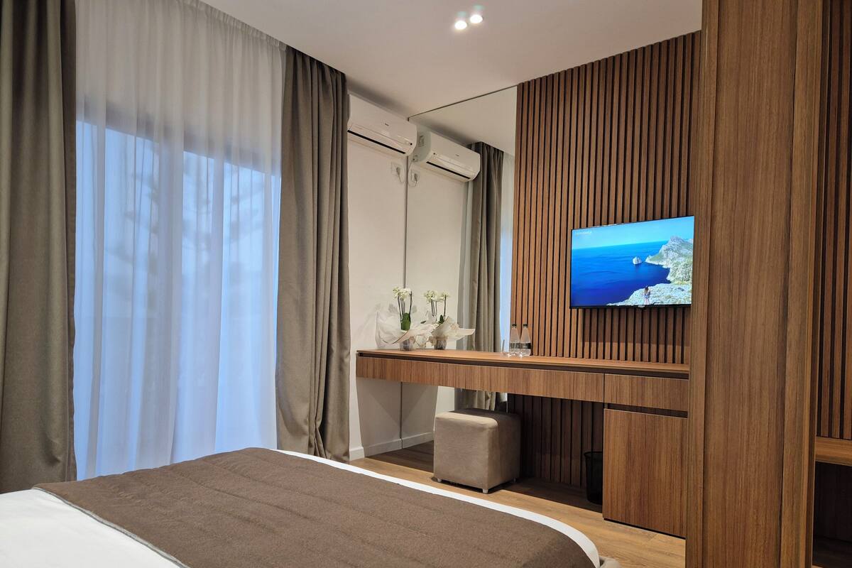 Una habitación de hotel moderna con una cama grande, un escritorio de madera, una televisión y vista al mar.