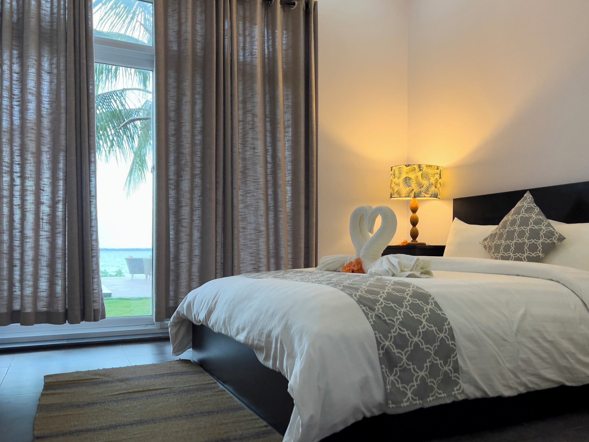 Una habitación de hotel con cama, mesita de noche, lámpara y vistas al exterior.