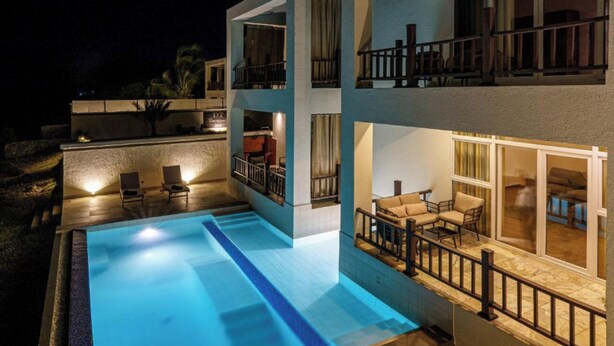 A modern multi-story building with a swimming pool, outdoor seating, and large windows. - DT Beachfront Villas (Fumba)