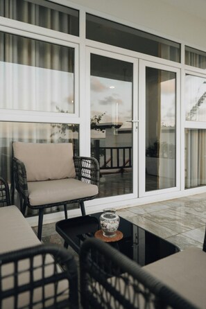 Una zona patio con un'area salotto che include una divisa e sedie, un tavolino con un oggetto decorativo e una porta vetrata che dà su uno spazio esterno.