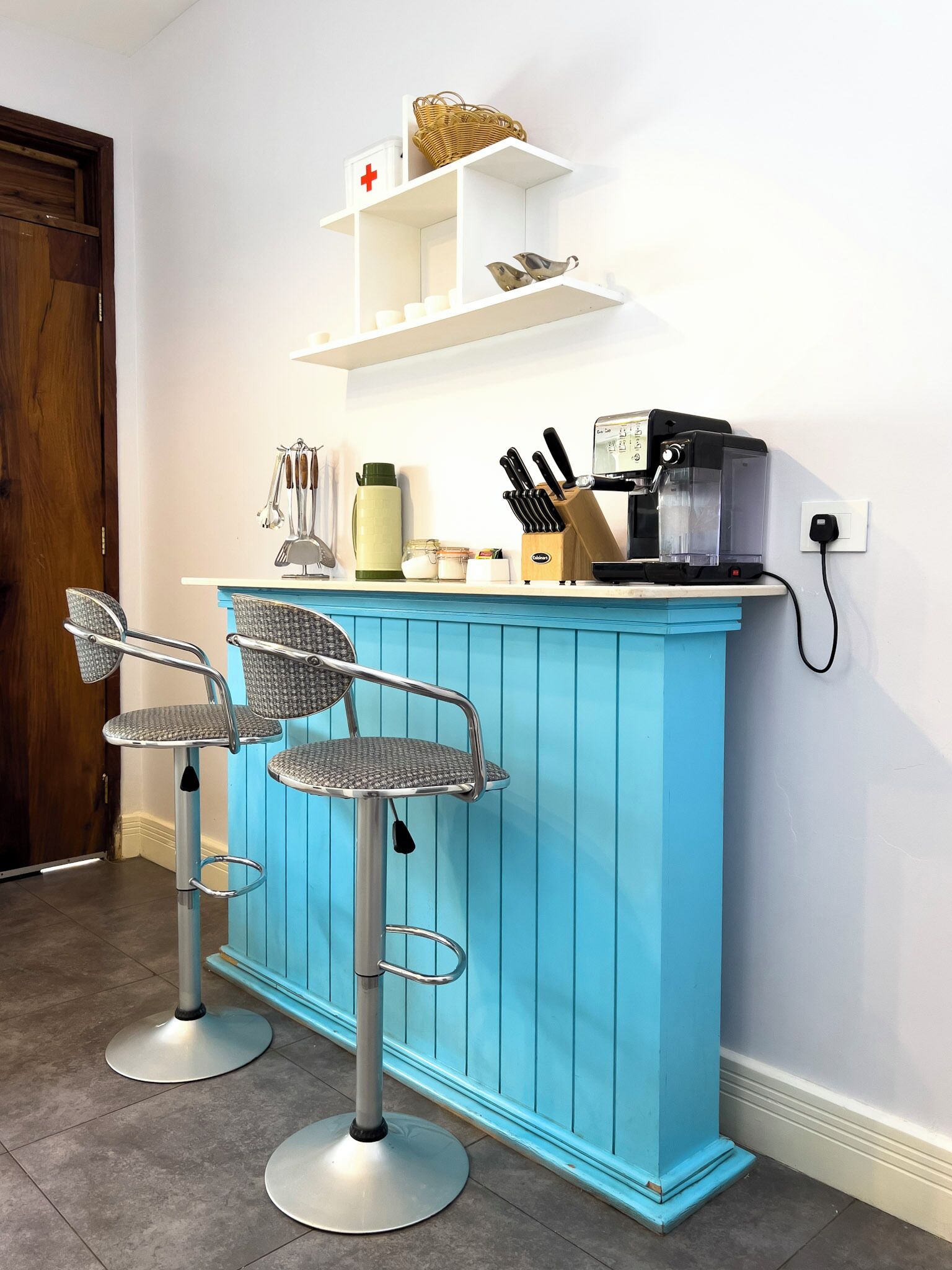 Un coin cuisine avec un comptoir de bar bleu, deux tabourets de bar, une machine à café et divers ustensiles de cuisine.
