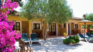 A courtyard with outdoor seating, a tree, and a building with a tiled roof. - SON MARGE (Campos)