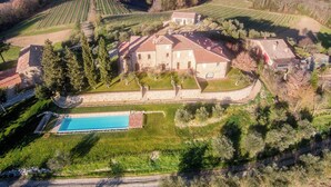 An aerial view of a large estate with a central building surrounded by vineyards, a swimming pool, and a well-maintained lawn.