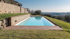 A rectangular swimming pool with clear blue water, surrounded by a stone wall and a brick deck.