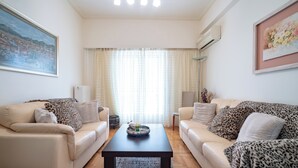 A living room with two beige sofas, a dark coffee table, and a large window with sheer curtains. - Piraiki Sea View Apt, 2bdrms, 4 pers by MPS (Pireas)