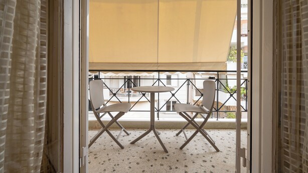 An open balcony with a table and two chairs, a yellow awning, and a view of the building's exterior. - Piraiki Sea View Apt, 2bdrms, 4 pers by MPS (Pireas)