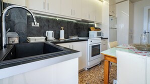 A modern kitchen with white cabinets, a black countertop, a stainless steel sink, a microwave, an oven, and a dining area with a glass table. - Piraiki Sea View Apt, 2bdrms, 4 pers by MPS (Pireas)