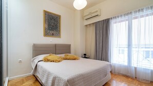 A bedroom with a large bed, a wall-mounted air conditioner, and a window with sheer curtains. - Piraiki Sea View Apt, 2bdrms, 4 pers by MPS (Pireas)