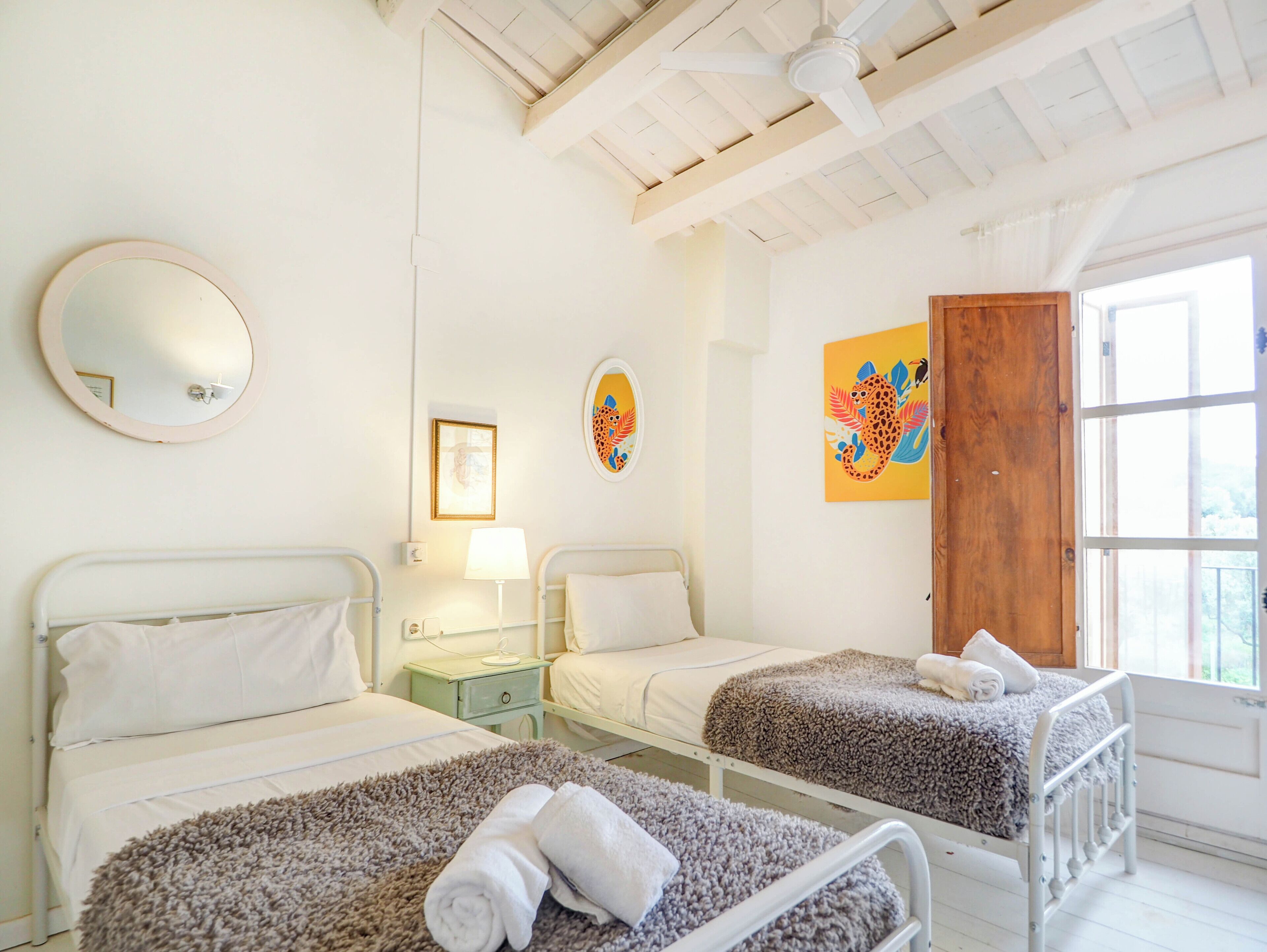 A hotel room with two beds, a round mirror, a wooden door, and artwork on the walls.