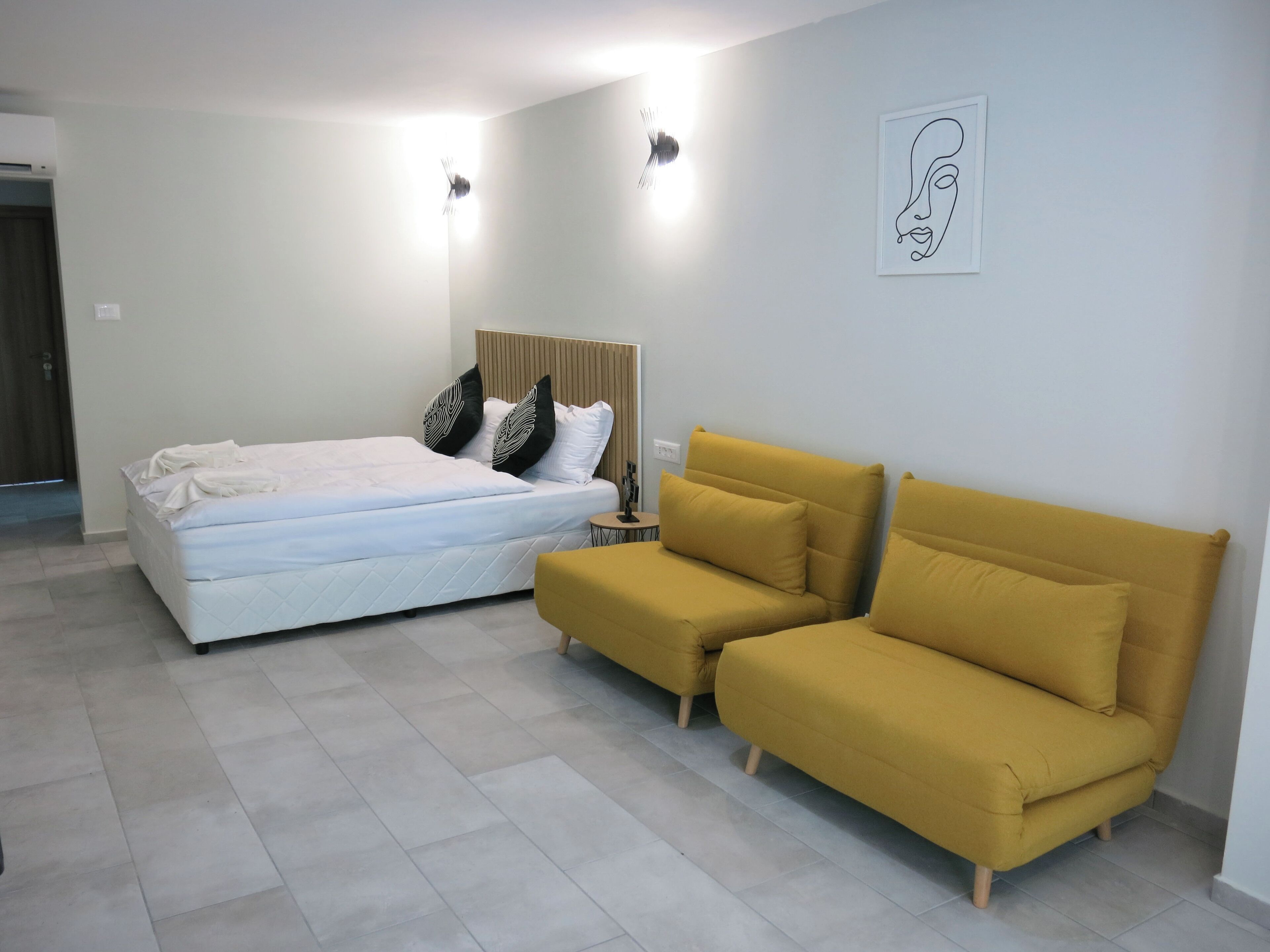 Ein Schlafzimmer mit einem Bett, einem gelben Sofa und einem an der Wand hängenden Kunstwerk.