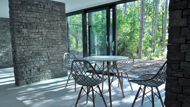 Un comedor moderno con pared de piedra, ventanas amplias y una mesa redonda con sillas.