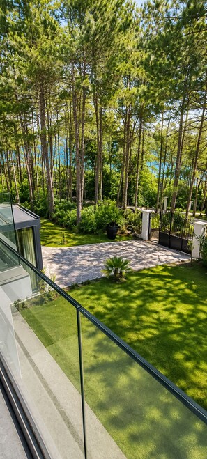 A modern outdoor area with a paved walkway, lush greenery, and a view of tall trees. - Hostel Teracite (Varna)