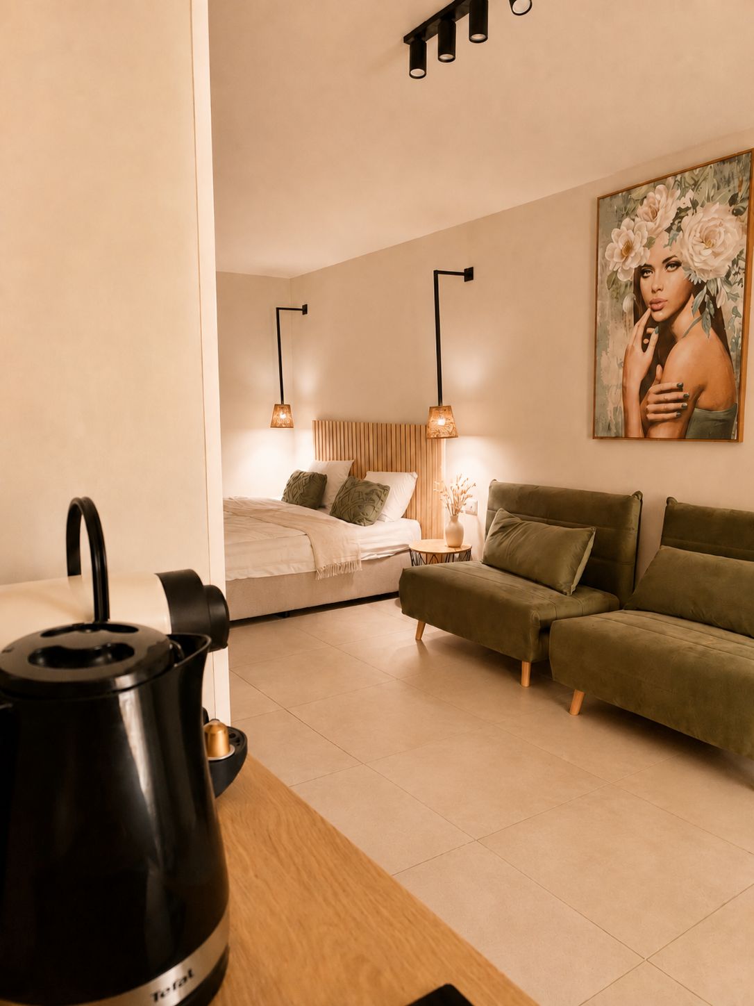 Un dormitorio moderno con una cama, un sofá verde, un cuadro y una tetera sobre una mesa.