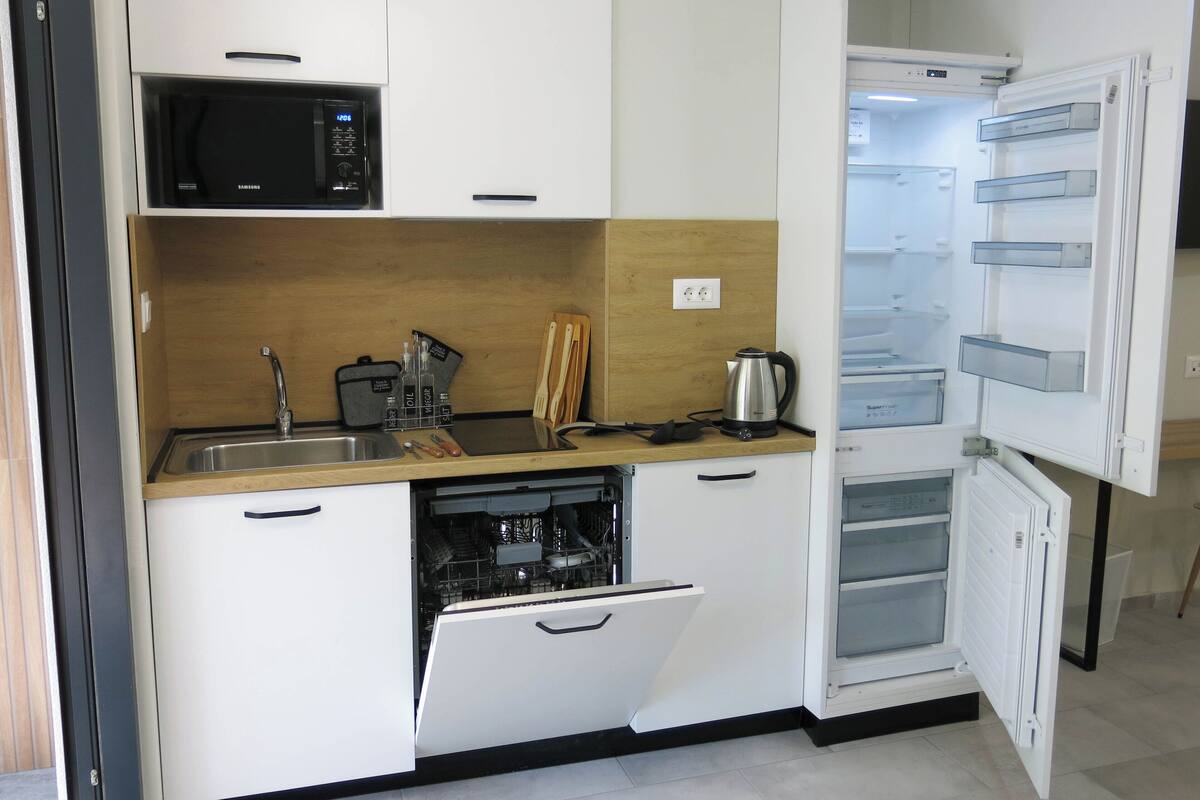 A compact kitchen with a microwave, kettle, and dishwasher.