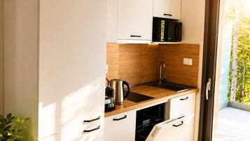 A compact kitchen with white cabinets, a microwave, a kettle, and a dishwasher.
