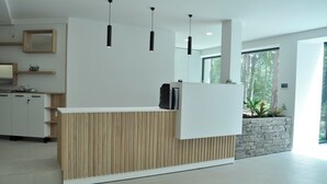 Una moderna zona de recepción con un mostrador de madera, una jardinera de piedra con plantas y un amplio ventanal con vistas a árboles.