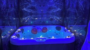 Una banyera d'hidromassatge amb un panell de control digital, envoltada per una habitació fosca amb un mural d'un arbre a les parets.