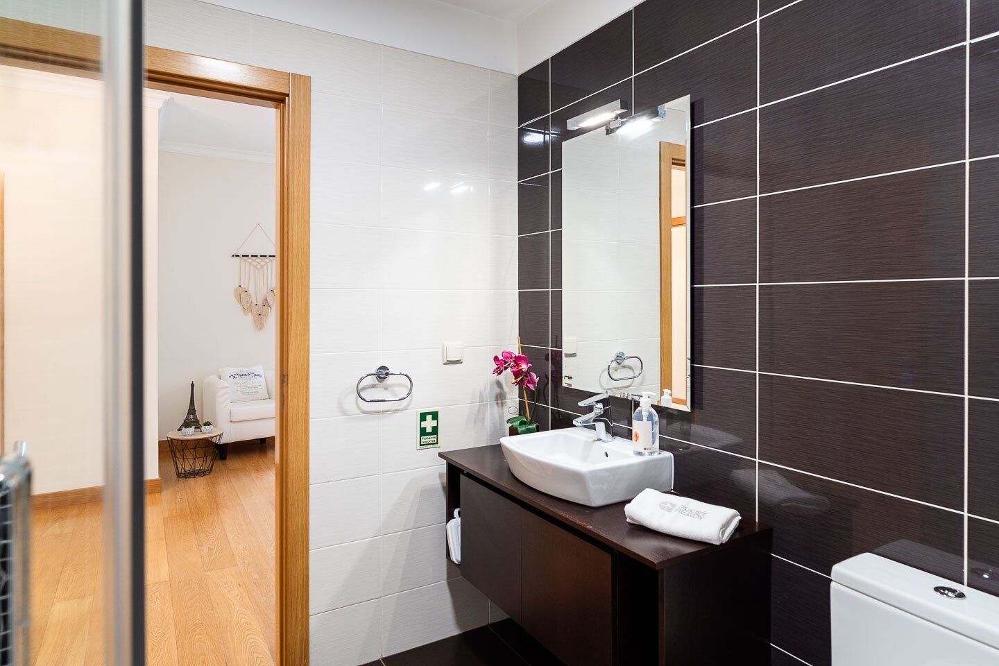Un baño moderno con un lavamanos blanco, paredes cubiertas de baldosas oscuras y una puerta de madera.