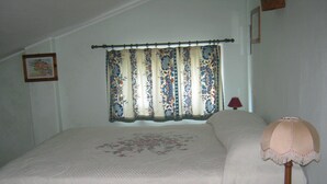 Un dormitorio con cama, mesita de noche, lámpara, ventana con cortinas e imagen enmarcada en la pared.