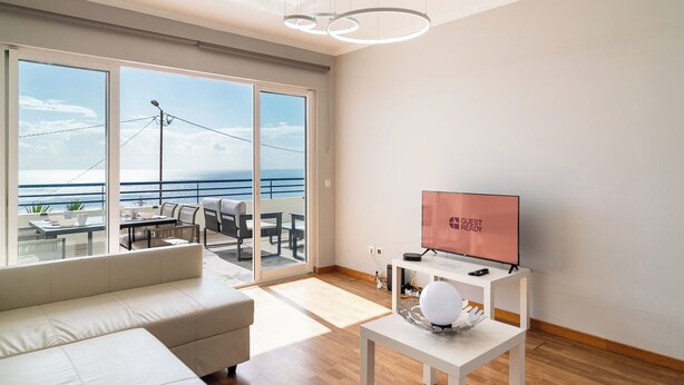 Un salon moderne doté d’une grande porte-fenêtre coulissante donnant sur un balcon avec vue sur la mer.