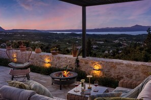 A patio with outdoor seating, a fire pit, and a scenic view of a lake and mountains. - Villa Anthos Crete - Superb Sea & hill Views w/ Private Pool, near Village & Sea (Gavalohori)