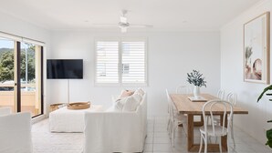 A bright, white interior with a dining area, a sofa, and a TV mounted on the wall. - Del Mar - 1 bed option (Shoal Bay)