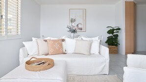 A modern living room with a white sofa, a matching ottoman, and a large potted plant. - Del Mar - 1 bed option (Shoal Bay)