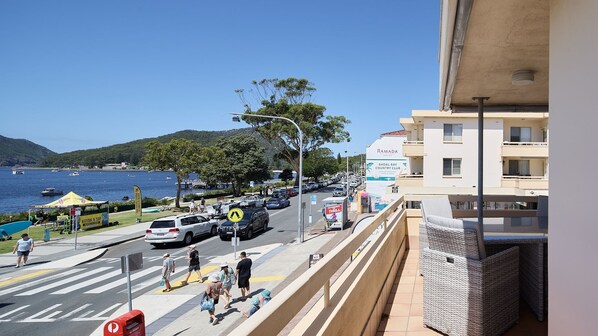 A coastal street with a view of the sea, parked cars, and a building with a sign for Ramada.
