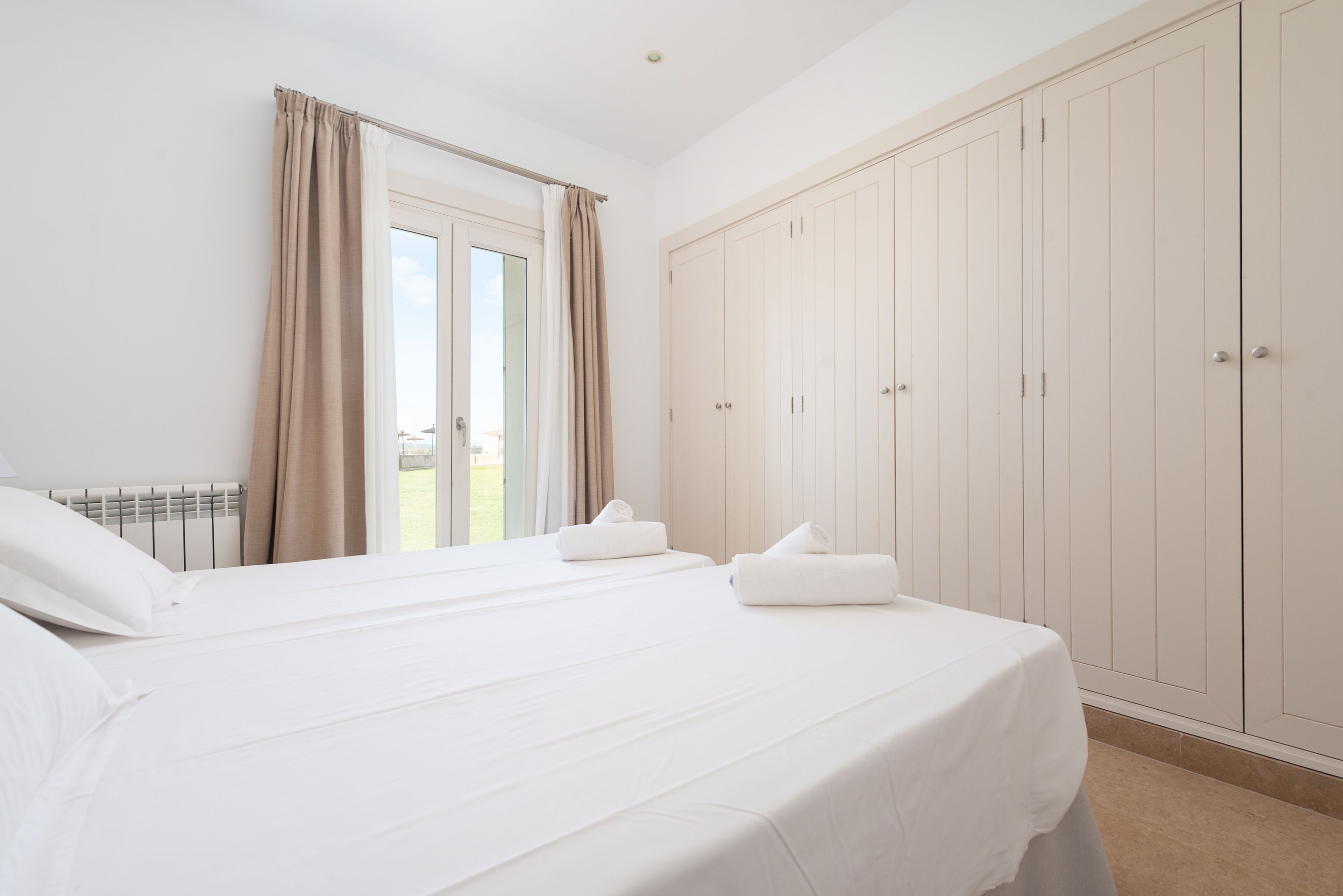 A bedroom with two beds, a large wardrobe, and a window with curtains.