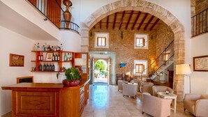 A spacious lobby with a wooden reception desk, a stone archway, and a staircase leading to an upper level. - Agritourism SA Franquesa Vella (Vilafranca de Bonany)