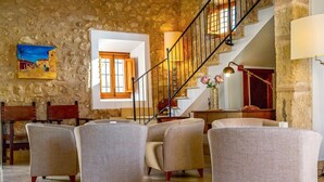 A spacious living area with a stone wall, a staircase, and comfortable seating. - Agritourism SA Franquesa Vella (Vilafranca de Bonany)