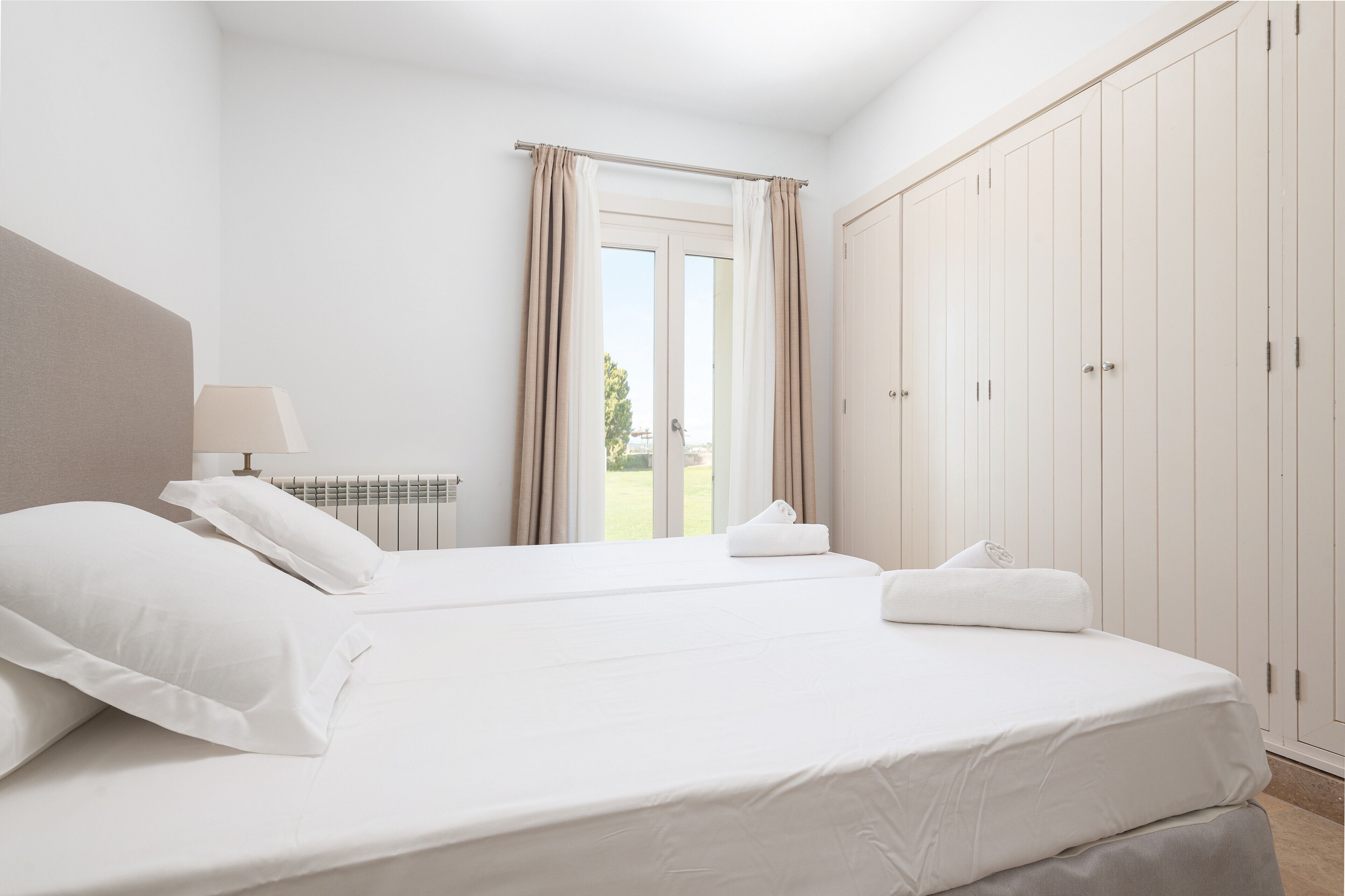 A hotel room with two beds, a radiator, a window with curtains, and a wardrobe.