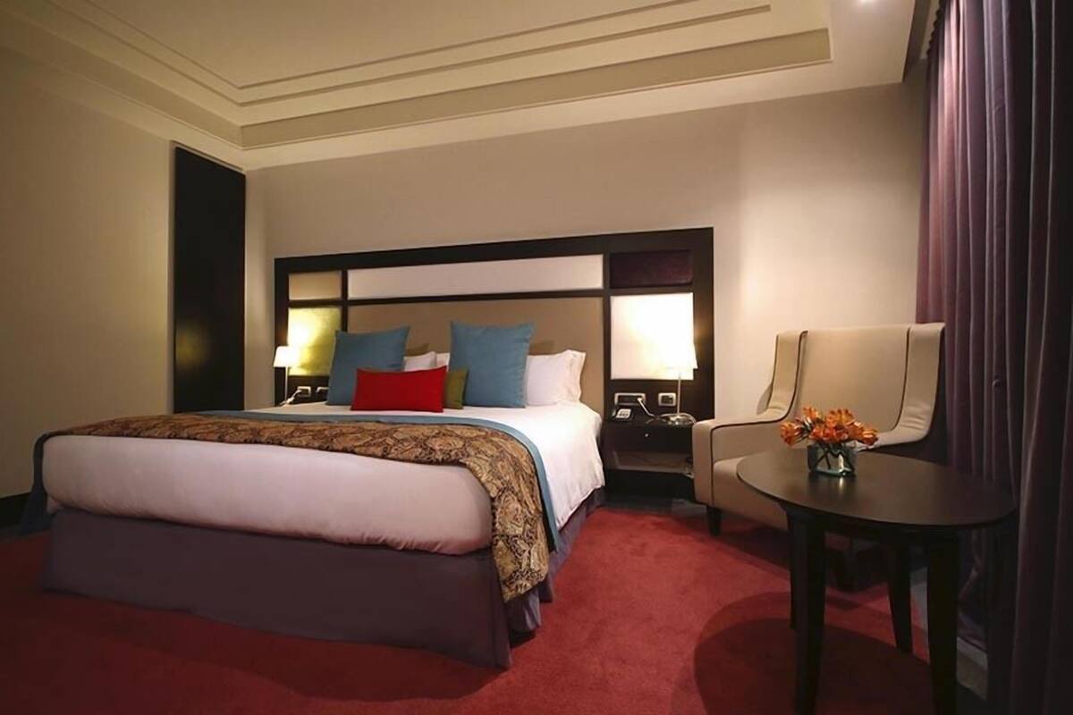Een hotelkamer met een groot bed, nachtlampen, een stoel en een tafeltje met bloemen.