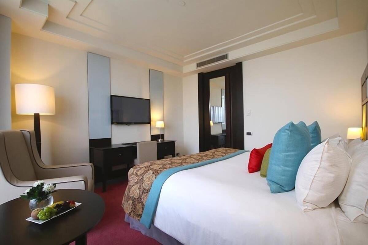 Hotelkamer met een bed, bureau, stoel, televisie en een eettafel met fruit.