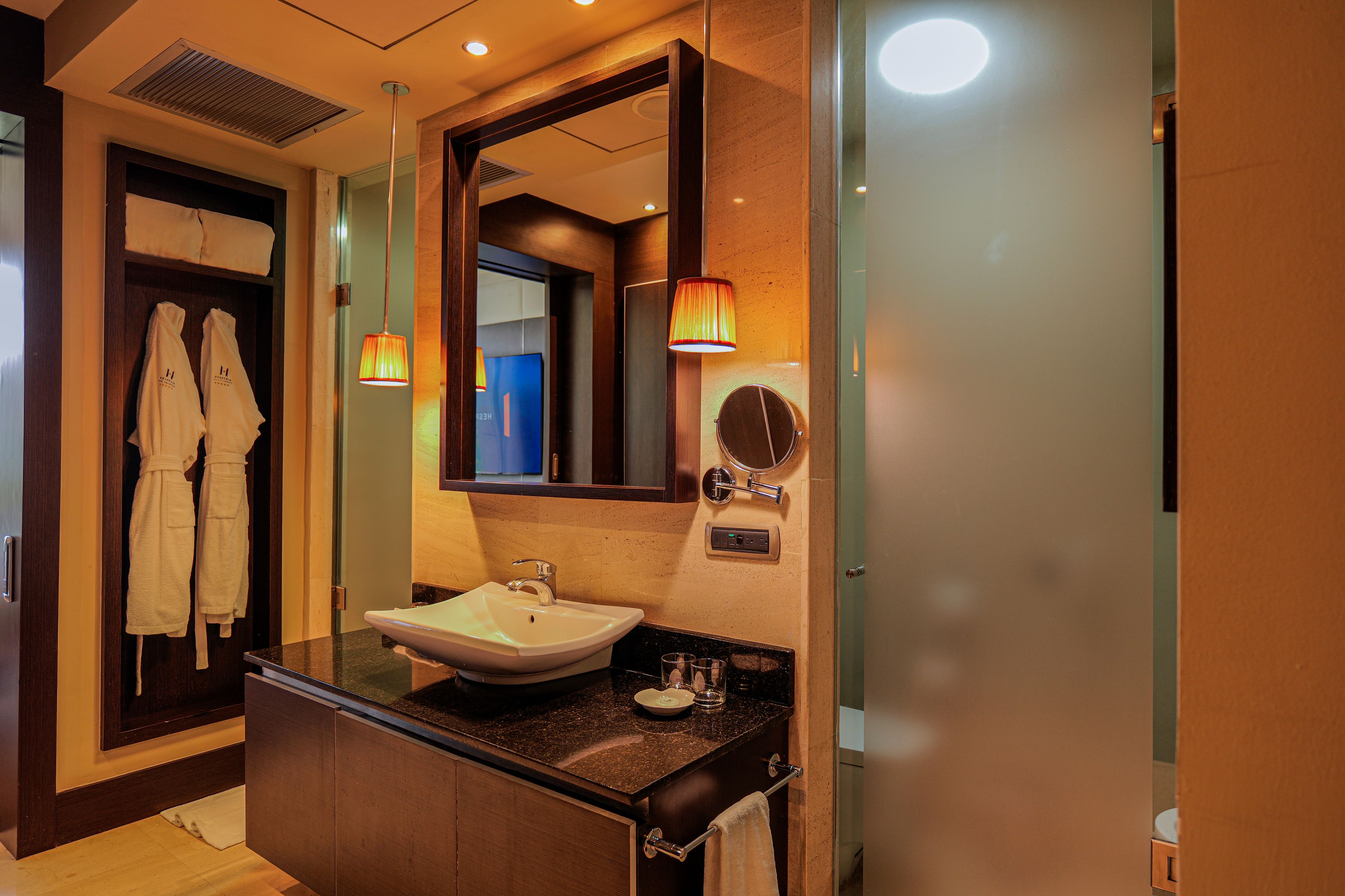 A modern bathroom with a vanity, sink, and mirror. There are towels hanging on a rack and a robe on a door.