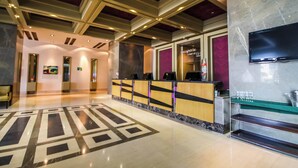 A hotel lobby with a reception desk, a television mounted on the wall, and a patterned floor. - Hotel Hesperia de Valencia (Naguanagua)
