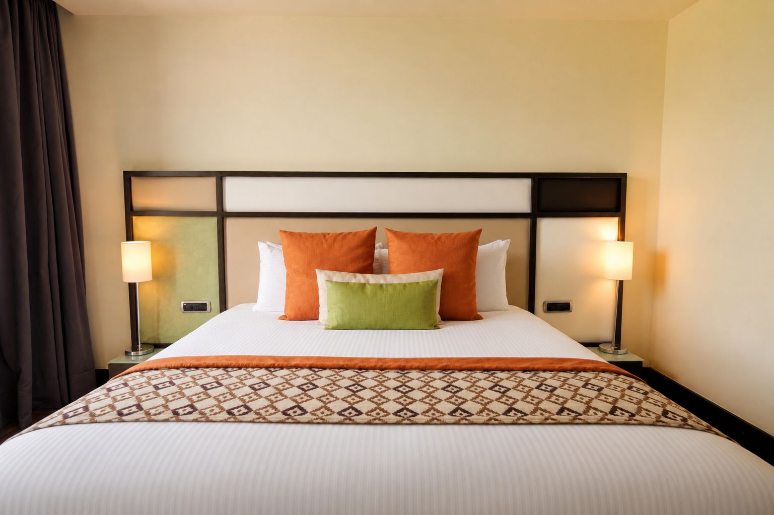 A hotel room with a large bed, two bedside lamps, and a patterned bedspread.