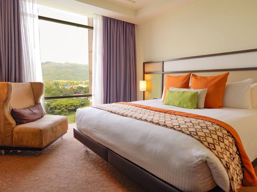A hotel room with a bed, a chair, and a view of the outdoors.