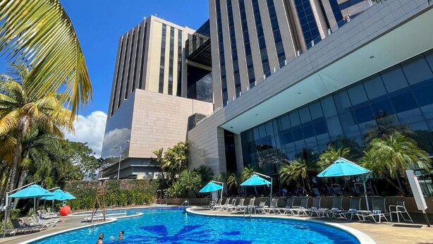 A modern hotel with a large swimming pool surrounded by palm trees and lounge chairs. - Hotel Hesperia de Valencia (Naguanagua)
