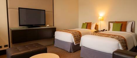 A hotel room with a television, two beds with pillows, a sofa, and a small round table.