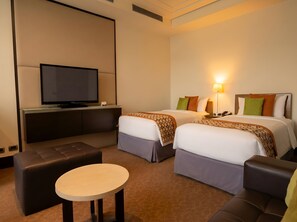 Una camera d'albergo con televisione, due letti con cuscini, un divano e un piccolo tavolino rotondo.