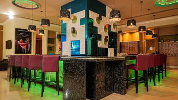 Un espace bar doté d’un comptoir en marbre, de plusieurs suspensions décoratives et de tabourets de bar.