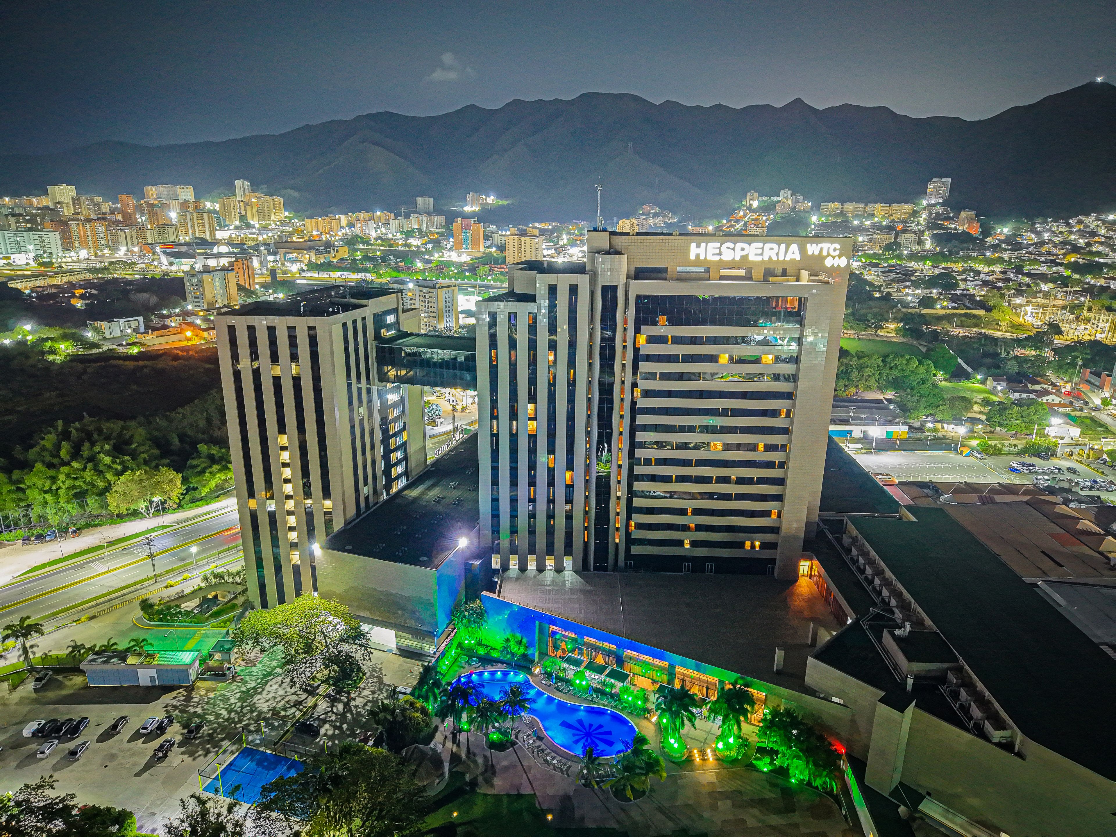A hotel with multiple high-rise buildings, a swimming pool, and a view of a cityscape with mountains in the background.