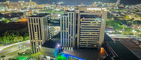 Un hotel con varios edificios altos, piscina y vista a un paisaje urbano con montañas al fondo.